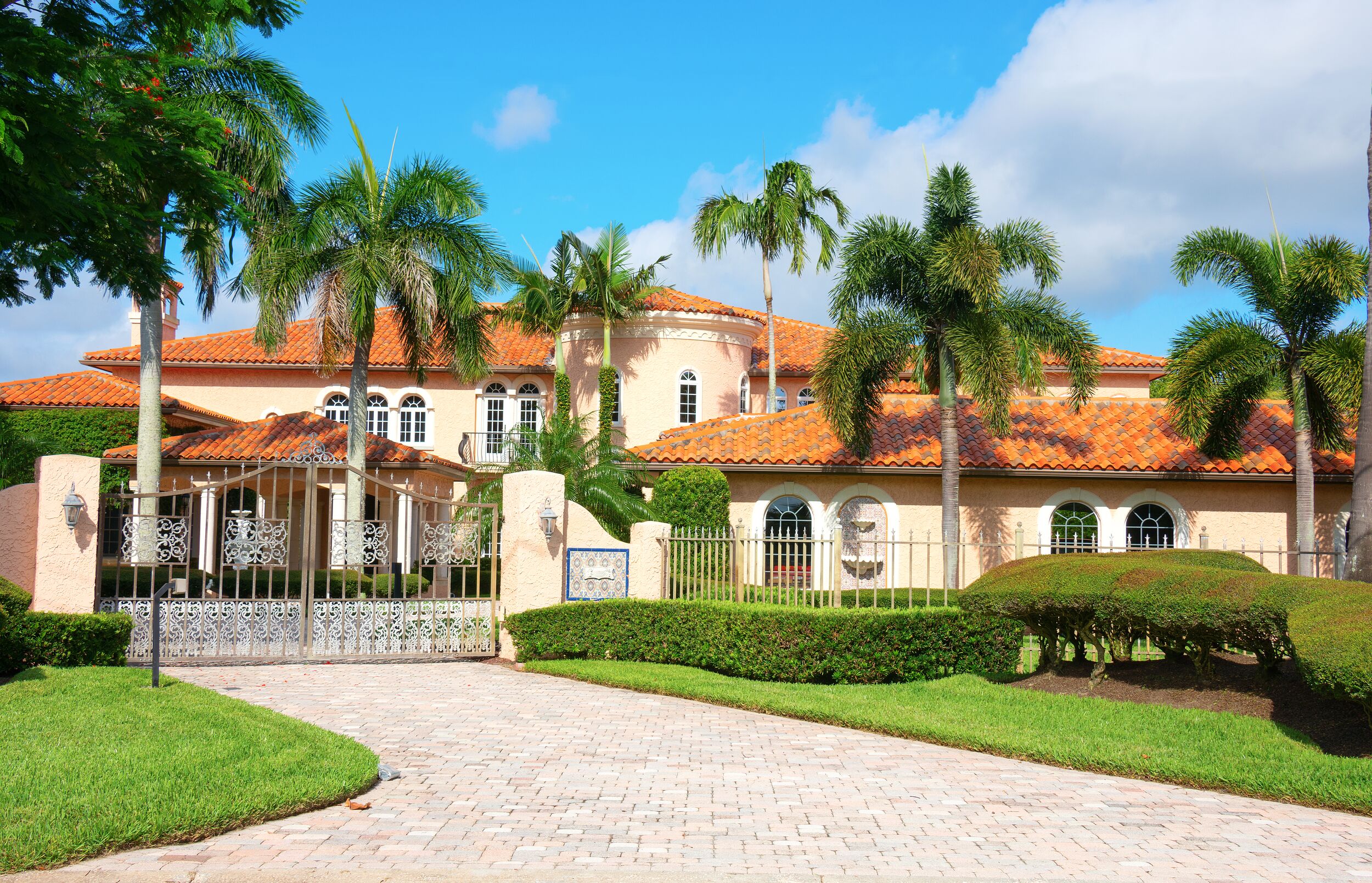 Beautiful Spanish style luxury mansion residential home with a privacy gate and palm trees on a blue sky sunny morning.