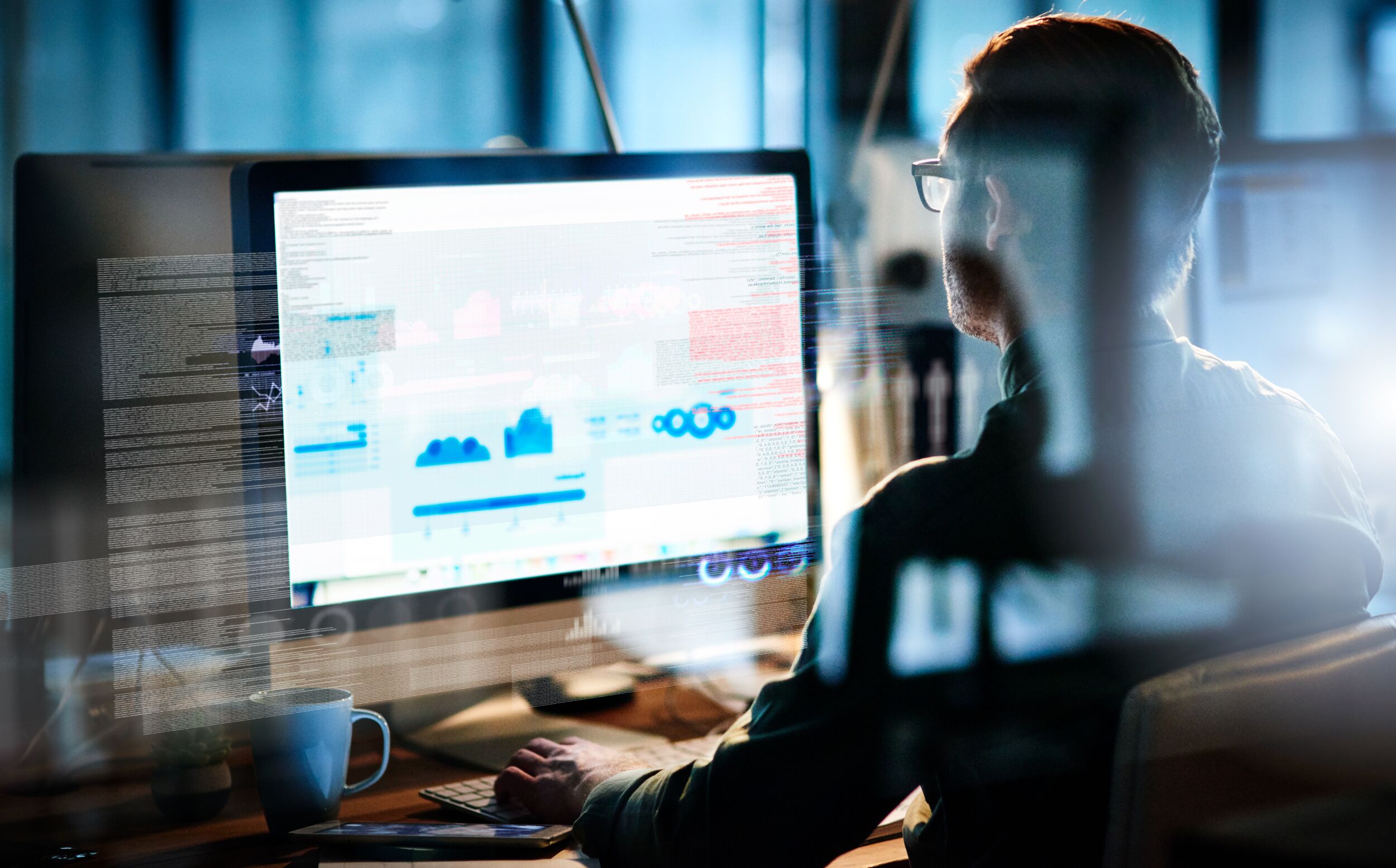 Man sitting in a dark office on a computer monitor.