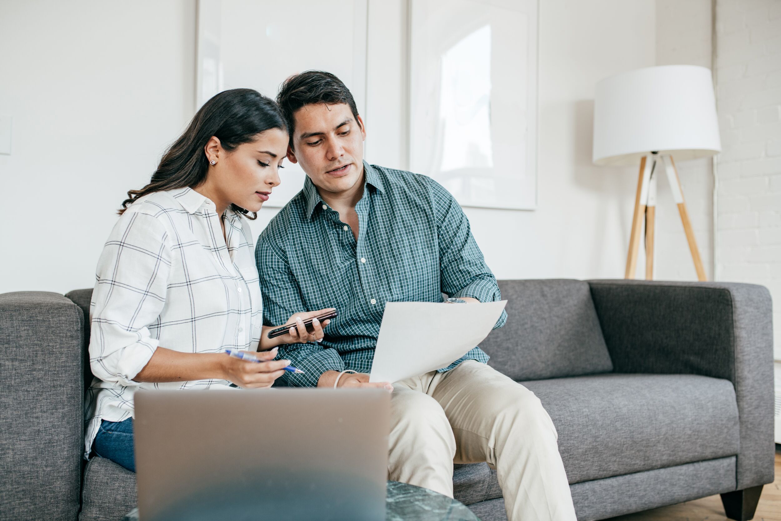 Couple looking on bank statements sitting on their living room couch.